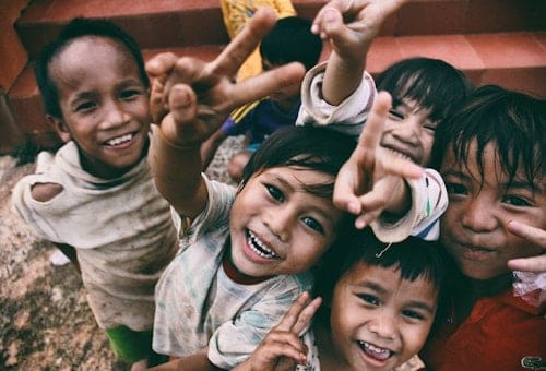 Một nhóm trẻ em cười tươi, giơ tay chào về phía máy ảnh.