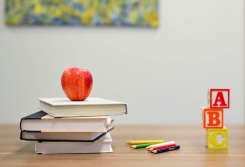 Chồng sách, quả táo đỏ và các khối chữ A B C trên bàn học.