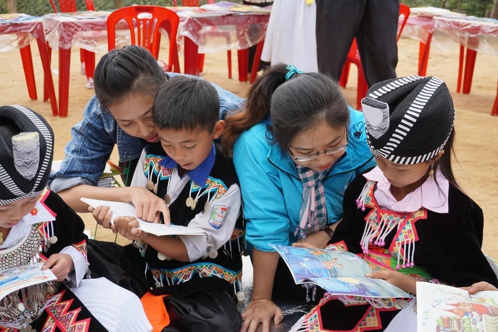 Các em nhỏ chụm đầu đọc sách cùng một cô giáo.