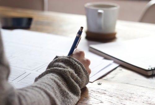 Một người đang viết ghi chú bên bàn làm việc.