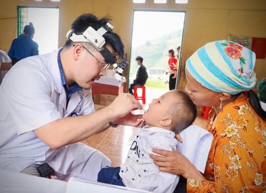 Một bác sĩ khám răng miệng cho em bé đang được người thân bế.